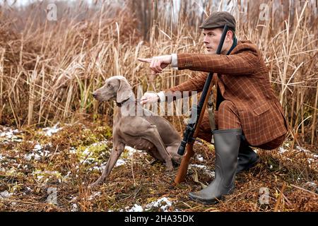 hunter und sein Hund auf der Suche nach Kleinwild, Mann zeigt zur Seite, geben Befehl an Hund. Starke graue Hund mit Besitzer auf der Jagd. Schöner Kerl selbstbewusst Klo Stockfoto