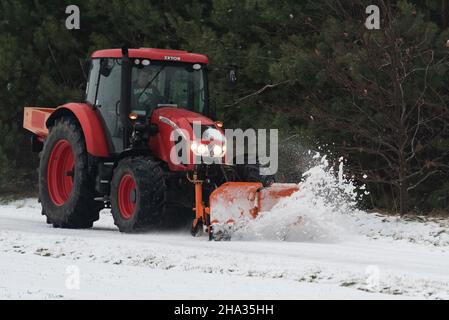 Pultusk, Polen - 10. Dezember 2021: Schneeräumung von einer Landstraße mit einem Traktor mit Schneepflug. Stockfoto