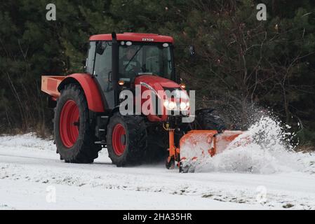 Pultusk, Polen - 10. Dezember 2021: Schneeräumung von einer Landstraße mit einem Traktor mit Schneepflug. Stockfoto