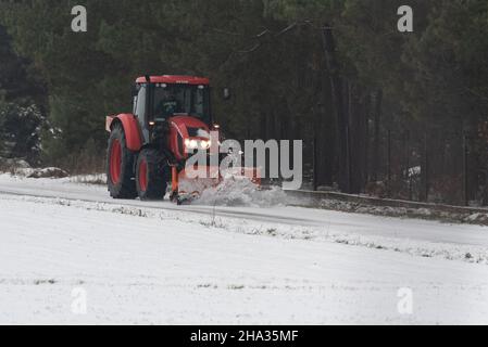 Pultusk, Polen - 10. Dezember 2021: Schneeräumung von einer Landstraße mit einem Traktor mit Schneepflug. Stockfoto