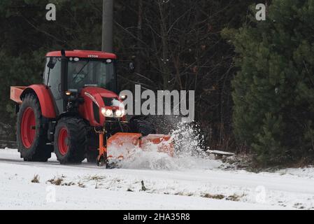 Pultusk, Polen - 10. Dezember 2021: Schneeräumung von einer Landstraße mit einem Traktor mit Schneepflug. Stockfoto