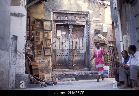 Eine lokale Frau an einer traditionellen Holztür in der Altstadt von Stone Town auf der Insel Sansibar in Tansania. Tansania, Sansibar, Stone Town, Oktober Stockfoto