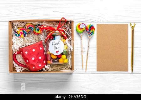 Handgemachtes Pflegepaket, saisonale Geschenkbox mit Süßigkeiten, Tasse auf weißem Tisch Personalisierter umweltfreundlicher Korb für Familie, Freunde, Mädchen für Danksagedanken Stockfoto