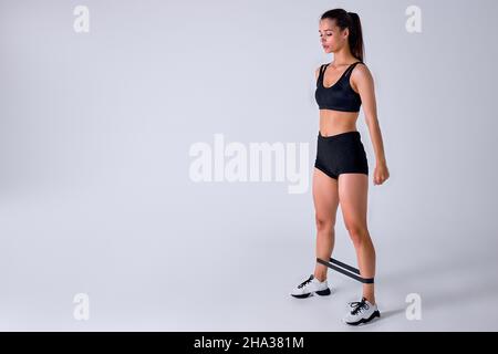 kaukasische Sportfitness Frau in Sportbekleidung mit Gummiband isoliert auf weißem Studio Hintergrund trainieren. Sportübungen, gesunder Lebensstil. St Stockfoto