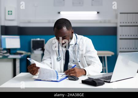afroamerikanischer Praktizierender Arzt Überprüfung Medizin verschreibungspflichtige Papiere Analyse pharmazeutischer Behandlung. Therapeut Mann arbeitet bei Patienten Krankheit Bericht im Krankenhaus Büro Stockfoto