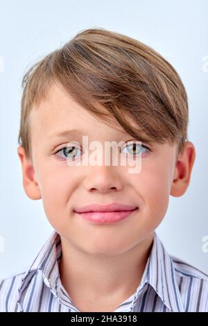 Kleiner Junge verbirgt Unzufriedenheit hinter einem Lächeln, gefälschte menschliche Emotionen Konzept. kaukasisches Kind im Hemd Blick auf die Kamera, mit blauen Augen. Porträt Stockfoto