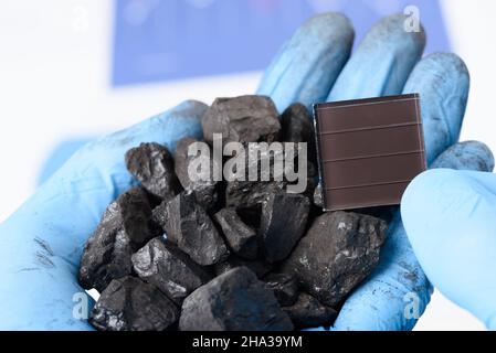 Eine Handvoll Kohle in der einen Hand und Solarpanel in der anderen. Übergang von fossilen Brennstoffen zu sauberem Energieforschungskonzept. Stockfoto