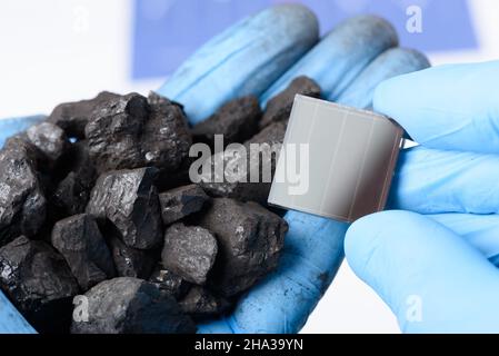 Eine Handvoll Kohle in der einen Hand und Solarpanel in der anderen. Übergang von fossilen Brennstoffen zu sauberem Energieforschungskonzept. Stockfoto