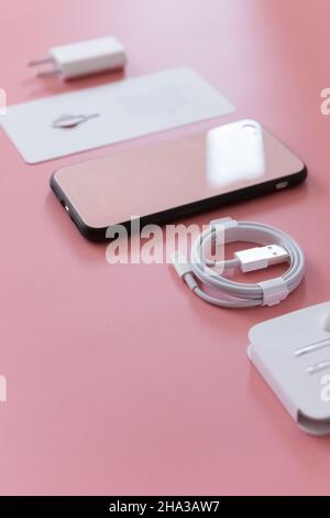 Flaches Lay von modernem Smartphone-Zubehör Ladegerät und Kopfhörer auf rosa Hintergrund Stockfoto