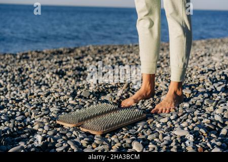 Eine Frau bereitet sich darauf vor, mit Nägeln auf einem Sadhu-Brett zu stehen, um am Meer zu üben. Stockfoto