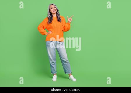 In voller Größe Foto von schönen weißen plus Größe alte Dame Index leeren Raum tragen Pullover Jeans Schuhe isoliert auf grünem Hintergrund Stockfoto
