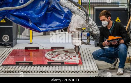 10. Dezember 2021, Sachsen, Chemnitz: Enrico Rudolph vom Forschungsbereich "Leichtbau im Bauingenieurwesen" der Technischen Universität Chemnitz verfolgt die Herstellung eines Betonschwungbogens im automatisierten 3D-Druckverfahren. Seit fünf Jahren forschen die Wissenschaftler am Institut für Leichtbau der Technischen Universität Chemnitz an automatisierten additiven Fertigungstechnologien. Vor kurzem präsentierten sie den weltweit ersten 3D-gedruckten Beton-Flying Buttress. Eine spezielle Faserbeton-Formel wird von einem Roboter in mehreren Schichten aufgetragen. T Stockfoto