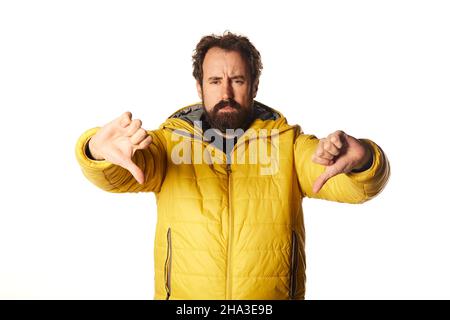 Bärtiger Mann, der traurig, enttäuscht oder wütend aussht, in Uneinigkeit den Daumen nach unten zeigt und frustriert ist. Stockfoto