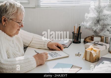 Gesunde Neujahrvorsätze für ältere Erwachsene. Ältere ältere alte Frau in weißem Pullover schreiben handgeschriebenen Text 2022 Ziele in offenen Notizblock auf dem Stockfoto