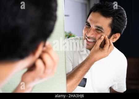 Fokus auf die Hand, trauriger Mann, der Gesicht überprüft und Pickel oder Akne vor dem Spiegel zu Hause drückt - Konzept der Hautpflege und Gesichtsinfektion Stockfoto