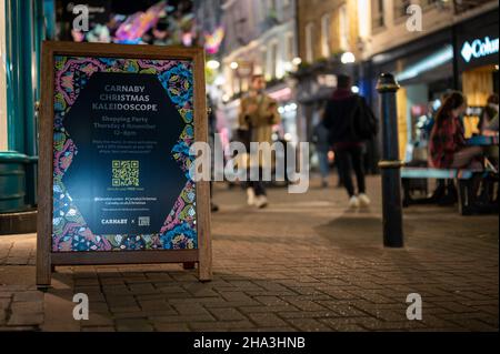 LONDON - 1. NOVEMBER 2021: Carnaby Street Weihnachtsbeleuchtung Werbung mit Käufern außerhalb des Fokus im Hintergrund Stockfoto
