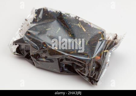 Schwarze Teepackung auf weißem Hintergrund. Tee mit langen Blättern und Rosenhüften, Äpfeln und Blütenblättern, verpackt in einer transparenten Verpackung. Tee mit Fruchtigkeit Stockfoto