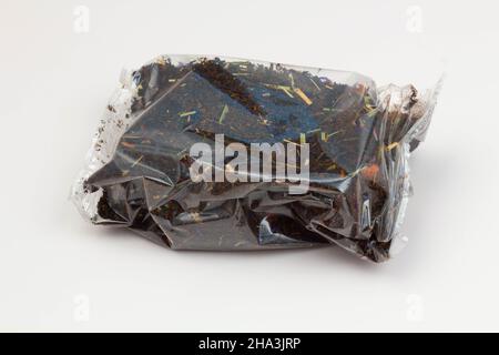 Schwarze Teepackung auf weißem Hintergrund. Tee mit langen Blättern und Rosenhüften, Äpfeln und Blütenblättern, verpackt in einer transparenten Verpackung. Tee mit Fruchtigkeit Stockfoto