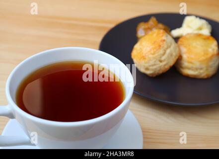 Nahaufnahme einer Tasse heißen Tee mit verschwommenen Scones im Hintergrund Stockfoto