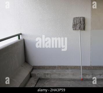 Ein schmutziger Mob oder Tupfer lehnt sich an eine Betonwand. Stockfoto