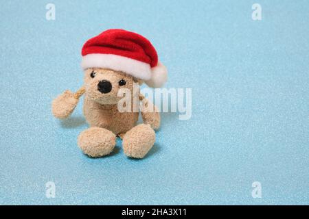 Gefüllter Teddybär in einem Weihnachtsmannhut auf blauem Hintergrund Stockfoto