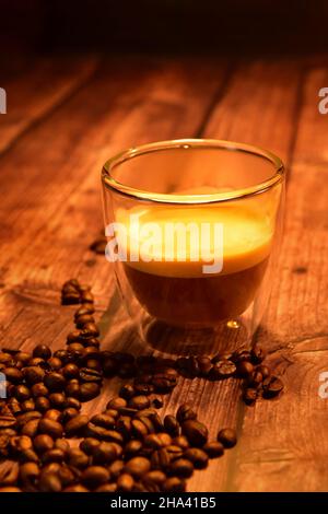 Vorderansicht einer Glastasse mit köstlichem Kaffee auf einem rustikalen Holztisch mit Kaffeebohnen. Stockfoto