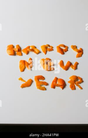 Unschärfe-Effekt Neujahrs-Wort, dargestellt durch orange trockene Schale auf grauem Hintergrund. Dekoration für Silvester, Konzept. Grußkarte. Text und DIY-Briefe. Stockfoto