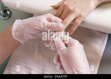 Nahaufnahme Nagelpflege durch Maniküre Spezialist im Schönheitssalon. Manikuristen reinigen die Nagelhaut mit professionellen Maniküre- und Pediküre-Zangen mit Handschuhen. Hand- und Nagelpflegekonzept Stockfoto