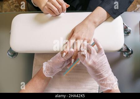 Nahaufnahme einer Frau im Nagelstudio, die eine Maniküre von der Kosmetikerin mit Nagelfeile macht. Frau macht Maniküre aus Nägeln. Die Kosmetikerin legt Nägel auf den Kunden. Professionelle Maniküre. Im Nagelstudio. Stockfoto