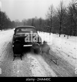 Polska, 1970. Dzieci na sankach przyczepionych do samochodu Wo³ga GAZ-21 na zaœnie¿onej drodze. ³p PAP/Edmund Uchymiak Dok³adny miesi¹c i dzieñ wydarzenia nieustalone. Polen, 1970. Kinder auf einem Schlitten, der am Wolga GAZ-21 Auto auf einer schneebedeckten Straße befestigt ist. lp PAP/Edmund Uchymiak Stockfoto