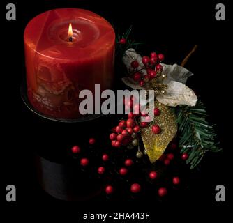 Schöne Weihnachtsdekoration mit brennender roter Kerze, roten Beeren und goldenem Blatt auf reflektierendem, glänzend schwarzem Hintergrund Stockfoto