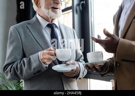 Beschnittene Ansicht eines älteren Geschäftsmannes, der während der Kaffeepause in der Nähe eines afroamerikanischen Kollegen stand Stockfoto