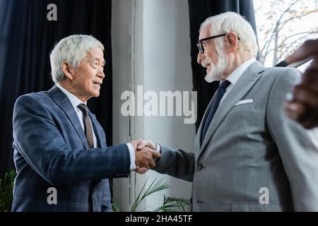Ältere interrassische Geschäftspartner lächeln, während sie im Büro die Hände schütteln Stockfoto