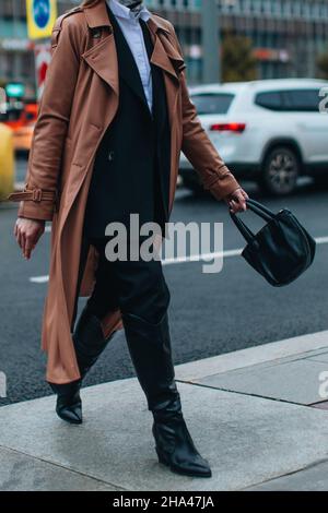 Verkürzte Figur einer Frau im langen braunen Ledermantel im Herbst und schwarzem Blazer, der in der Stadt unterwegs ist. Street Style, lässige Damenmode Stockfoto