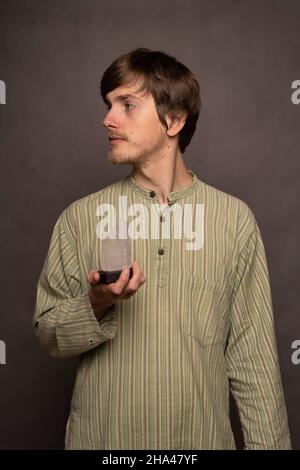Junger, hübscher, großer, schlanker weißer Mann mit braunem Haar und Kristall, der links in einem gestreiften Hemd auf grauem Hintergrund aussieht Stockfoto