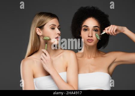 Interracial Frauen mit perfekter Haut mit Jadewalzen isoliert auf grau Stockfoto