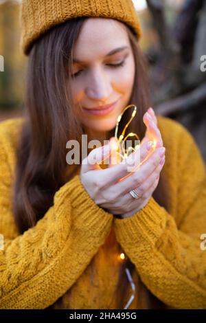 Weiße junge europäische Frau in gelben Pullover Porträt hält Lichter in den Händen Stockfoto