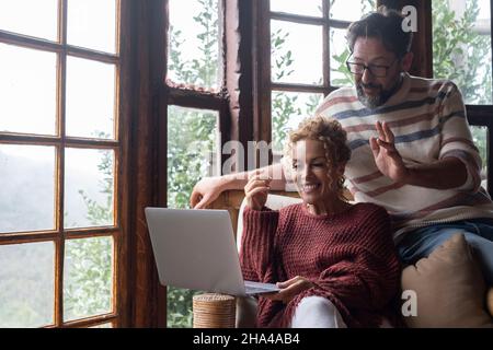 Glücklich und aufgeregt Paar Mann und Frau machen Videokonferenz mit Freunden oder Parentes zu Hause mit Laptop-Computer und Internet-WLAN-Verbindung. Glückliche Menschen nutzen Technologie in Indoor-Freizeit Stockfoto