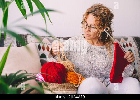 Erwachsene attraktive Frau zu Hause in Stricken Arbeit Tätigkeit mit bunten Wolle. Glückliche und entspannte weibliche Menschen genießen Zeit in der Halle auf dem Sofa. Strick Job Stockfoto