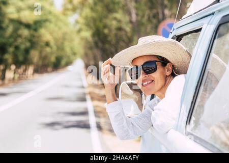 Fröhliche Frau in Sonnenbrille und Hut Blick außerhalb Auto aus dem Fenster. Junge Frau genießen Urlaub auf Roadtrip. Lächelnde Frau bewundern die Natur, während aus dem Auto Fenster Stockfoto