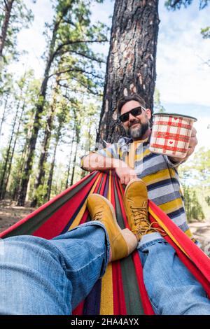 Glücklicher Erwachsener kaukasischen Paar genießen Sie die Natur Outdoor-Freizeit Camping-Aktivität - Frau Beine pov auf Hängematte und Mann mit Kaffee stehen - Umwelt und Natur Urlaub Stockfoto