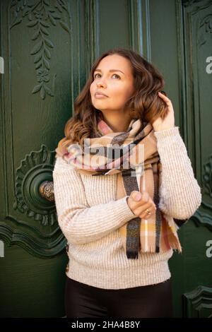 Europäische weiße junge Frau mit braunem Haar in einem Schal in der Nähe der alten Tür, die ihr Haar berührt Stockfoto