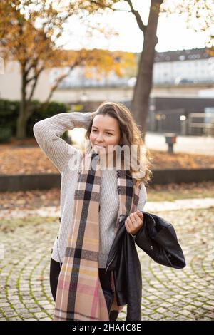 Lächelnde weiße junge europäische Frau mit braunen Haaren, die im Herbst die Hand hinter ihrem Kopf hält Stockfoto