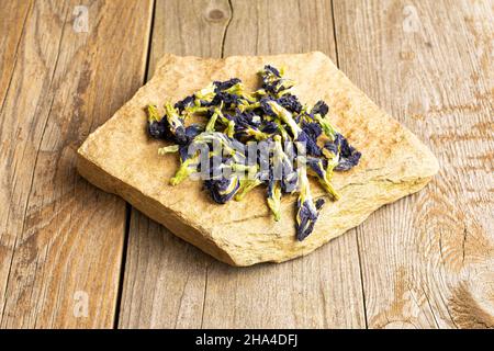 Viele ganze trockene clitoria ternatea mit natürlichem flachen Felsen auf altem Holz Stockfoto