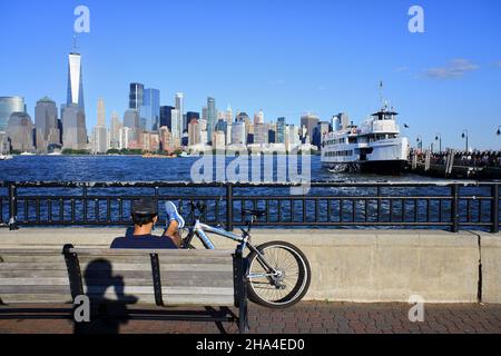 Ein Besucher, der sich mit seinem Fahrrad im Liberty State Park mit dem Hudson River und der Skyline von New York City im Hintergrund entspannt.New City.New Jersey.USA Stockfoto