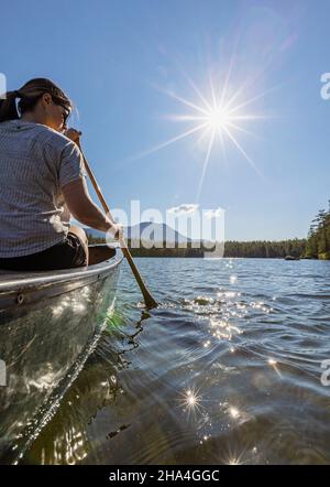 Junge Frau paddelt Kanu auf Daicey Pond, Maine. Katahdin in der Ferne. Stockfoto