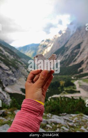 Frau hält ein Steinherz in die Kamera, über dem reintal unterhalb der knorr-Hütte, bei garmisch-partenkirchen mit Blick auf die Reintalangerhütte, garmisch-partenkirchen, wettersteingebirge, bayern, deutschland, europa Stockfoto