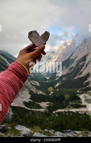 Frau hält ein Steinherz in die Kamera, über dem reintal unterhalb der knorr-Hütte, bei garmisch-partenkirchen mit Blick auf die Reintalangerhütte, garmisch-partenkirchen, wettersteingebirge, bayern, deutschland, europa Stockfoto