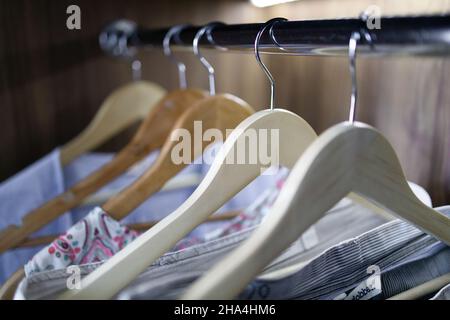 Farbige Kleidung hängt auf einem Kleiderständer in einem Holzschrank mit Beleuchtung im Haus Stockfoto