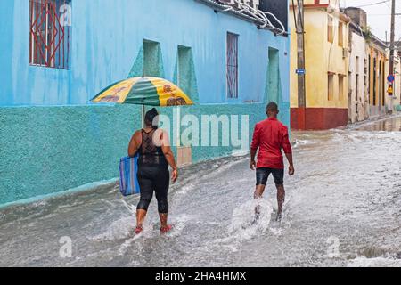 Kubaner mit Sonnenschirmen wandern in der Stadt Santiago de Cuba auf der Insel Kuba, Karibik, in überfluteter Straße bei sintflutartigen Regenfällen Stockfoto